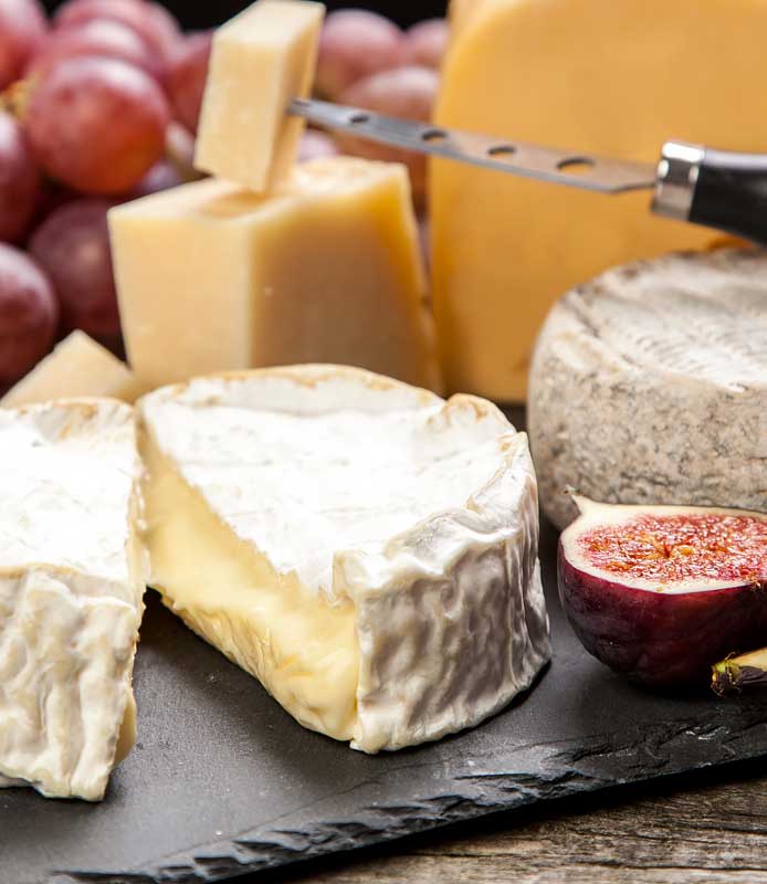 Selección de quesos junto a unas uvas e higos sobre una tabla de cortar.